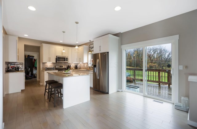 kitchen with tasteful backsplash, white cabinets, decorative light fixtures, a kitchen island, and appliances with stainless steel finishes