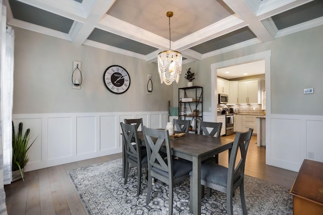 dining space with hardwood / wood-style flooring, coffered ceiling, crown molding, and an inviting chandelier