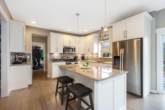 kitchen featuring pendant lighting, a kitchen island, stainless steel appliances, and light hardwood / wood-style flooring