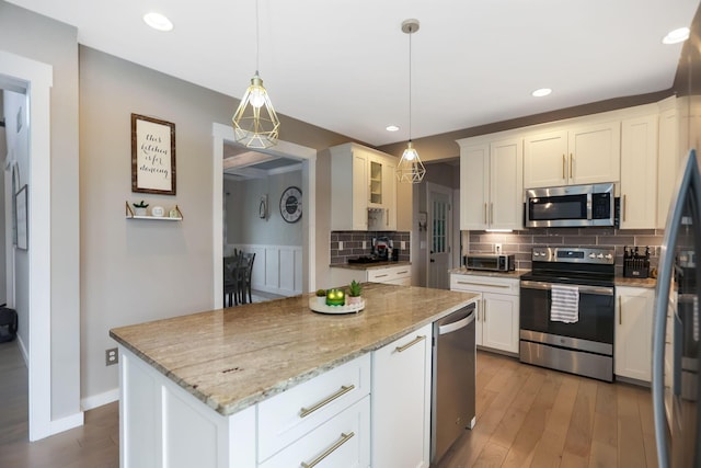 kitchen with light stone counters, white cabinets, stainless steel appliances, and decorative light fixtures