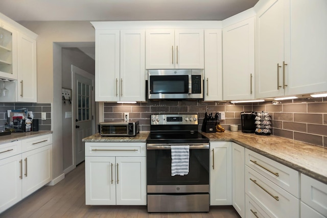 kitchen with white cabinets, appliances with stainless steel finishes, decorative backsplash, and light hardwood / wood-style floors