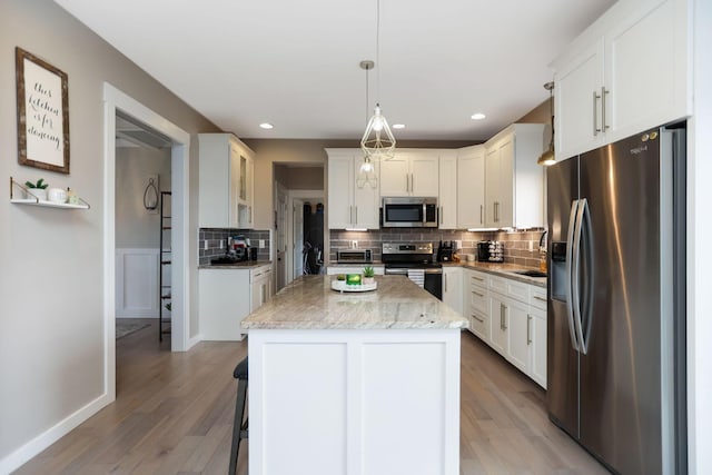 kitchen with a center island, white cabinets, light wood-type flooring, decorative light fixtures, and stainless steel appliances