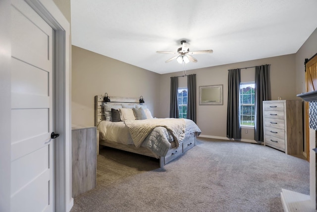 bedroom with ceiling fan, a barn door, and carpet floors