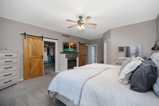 carpeted bedroom featuring a walk in closet, a barn door, a closet, and ceiling fan