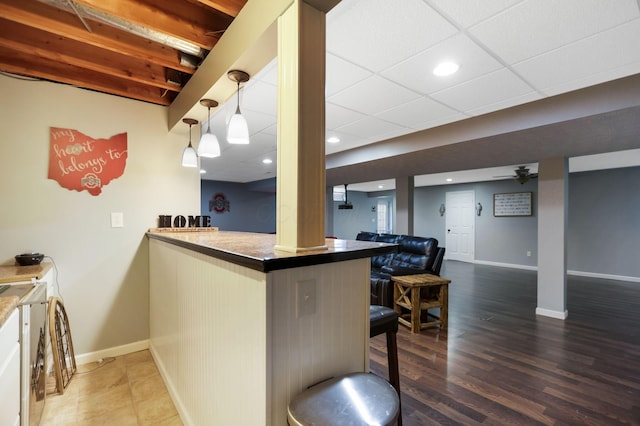 kitchen featuring dark wood-type flooring, kitchen peninsula, decorative light fixtures, a paneled ceiling, and a breakfast bar