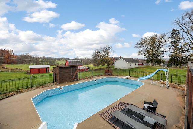 view of swimming pool featuring a patio, a lawn, a storage shed, and a water slide