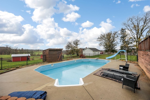 view of pool featuring a diving board, a patio area, a water slide, a storage unit, and a lawn