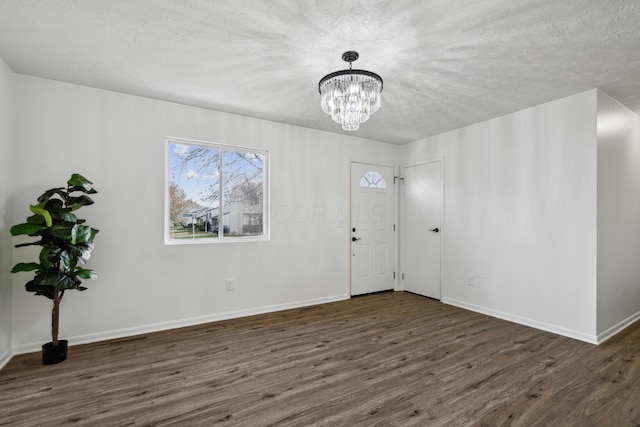 empty room featuring dark hardwood / wood-style flooring, a textured ceiling, and a chandelier