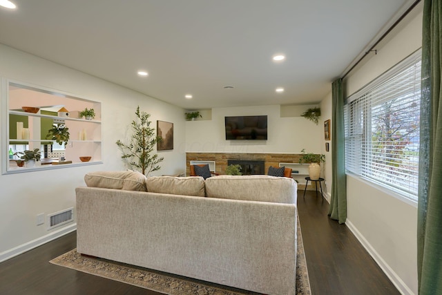 living room featuring a stone fireplace and dark hardwood / wood-style flooring