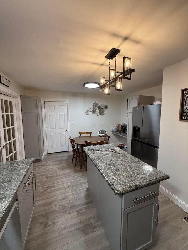 kitchen with appliances with stainless steel finishes, decorative light fixtures, a center island, gray cabinets, and dark hardwood / wood-style floors