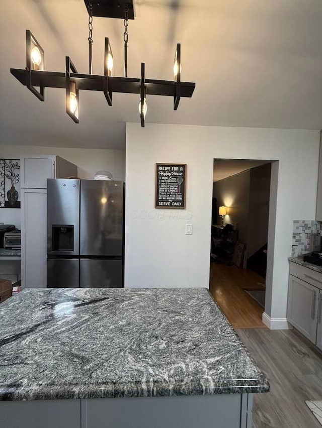 kitchen featuring hardwood / wood-style floors, dark stone counters, and stainless steel refrigerator with ice dispenser