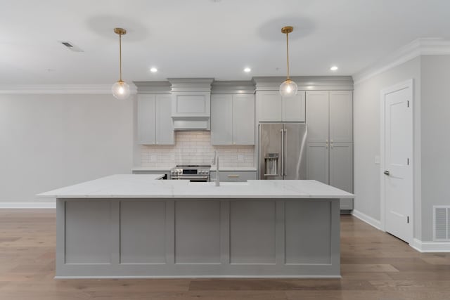 kitchen featuring a large island with sink, light stone counters, stainless steel appliances, and decorative light fixtures