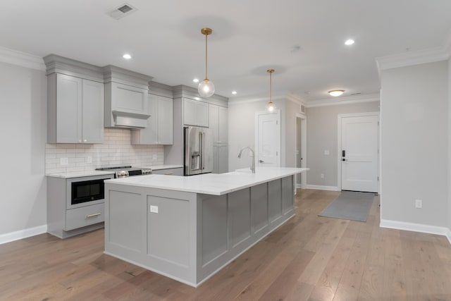 kitchen featuring gray cabinetry, a center island with sink, hanging light fixtures, light wood-type flooring, and appliances with stainless steel finishes