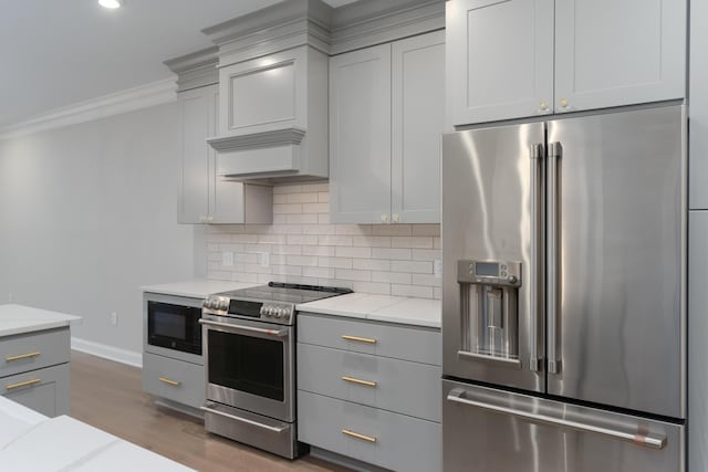 kitchen with hardwood / wood-style flooring, ornamental molding, tasteful backsplash, light stone counters, and stainless steel appliances