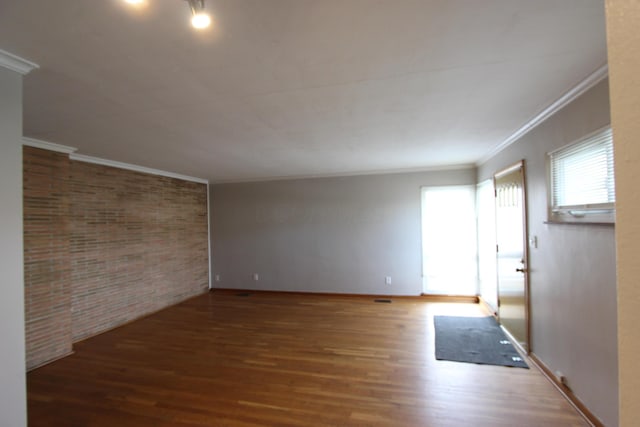 empty room with dark hardwood / wood-style floors, crown molding, and brick wall