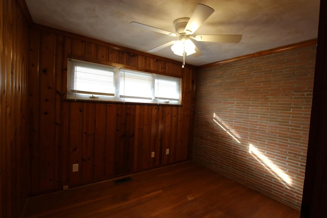 spare room featuring brick wall, hardwood / wood-style flooring, ceiling fan, and wood walls