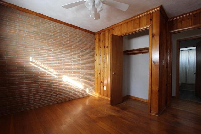 unfurnished bedroom with dark hardwood / wood-style flooring, ceiling fan, crown molding, a closet, and wood walls