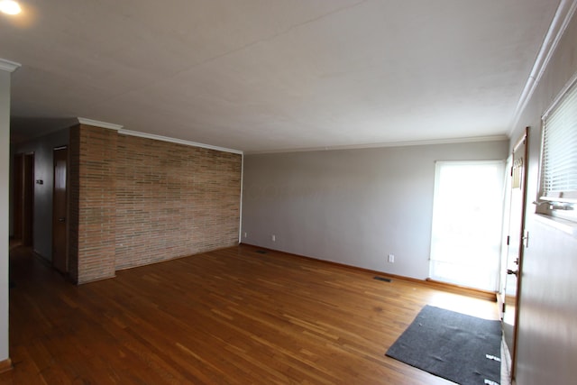 spare room featuring crown molding, dark hardwood / wood-style flooring, and brick wall