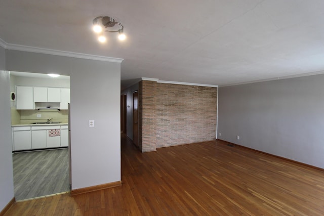 unfurnished living room featuring brick wall, dark hardwood / wood-style floors, ornamental molding, and sink