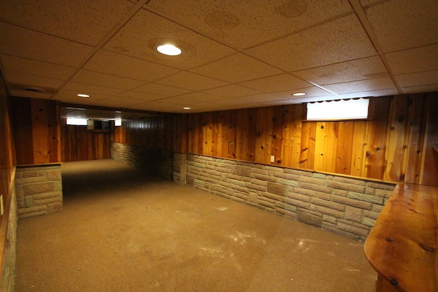 basement with a drop ceiling, wood walls, and carpet floors