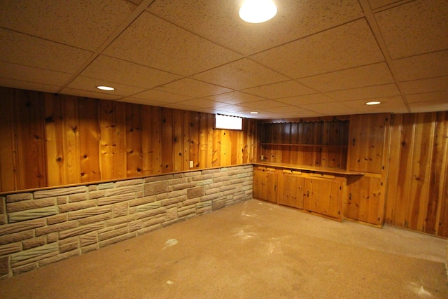 basement with carpet flooring, a paneled ceiling, and wooden walls