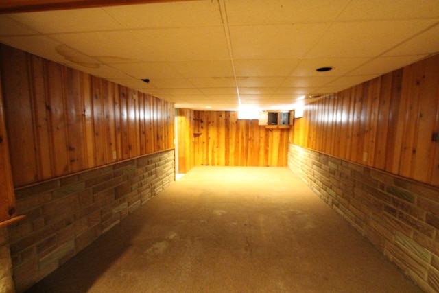 basement featuring carpet flooring, a drop ceiling, wood walls, and brick wall