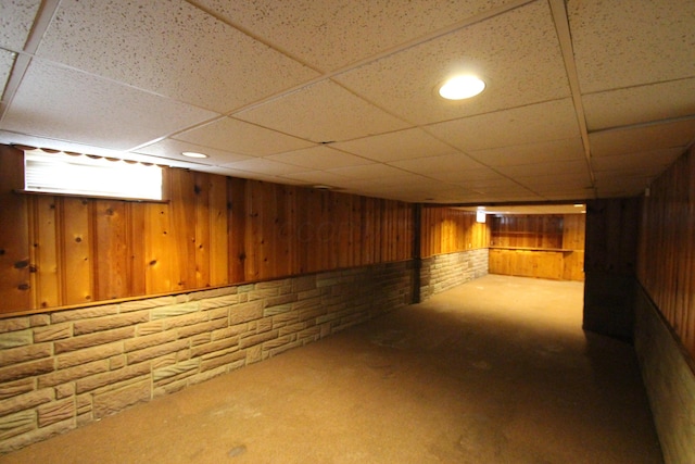 basement with carpet flooring, a drop ceiling, and wooden walls