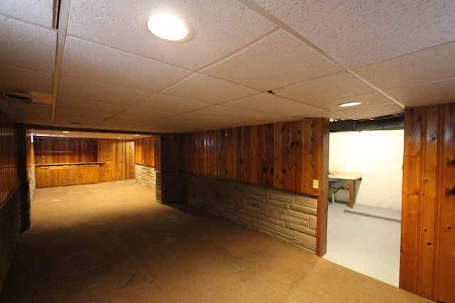 basement with a drop ceiling, wood walls, and carpet floors