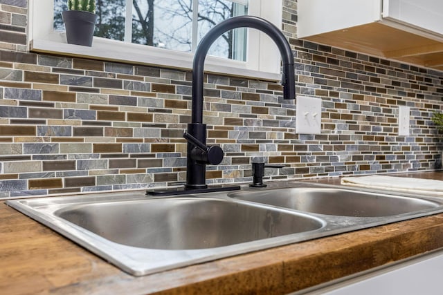 interior details with white cabinets, decorative backsplash, and sink