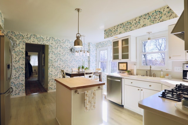 kitchen featuring light hardwood / wood-style floors, stainless steel appliances, white cabinets, butcher block countertops, and hanging light fixtures