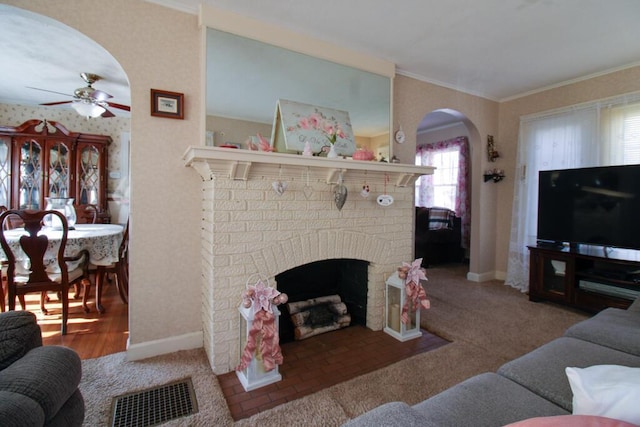 living room with ceiling fan, crown molding, hardwood / wood-style flooring, and a brick fireplace