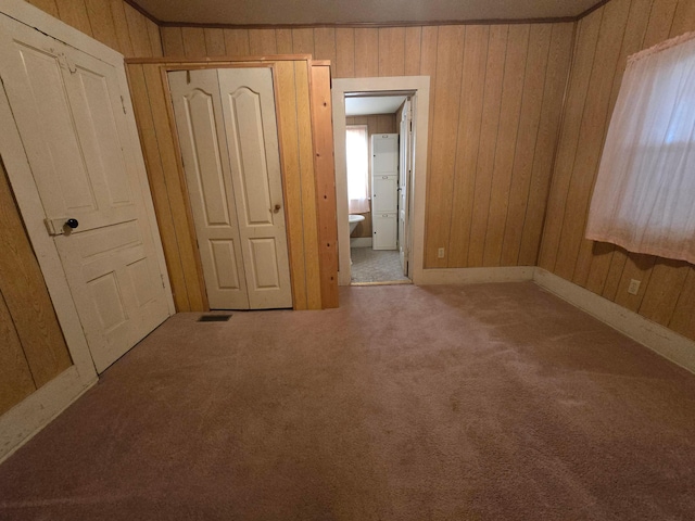 unfurnished bedroom featuring carpet flooring, a closet, ornamental molding, and wood walls