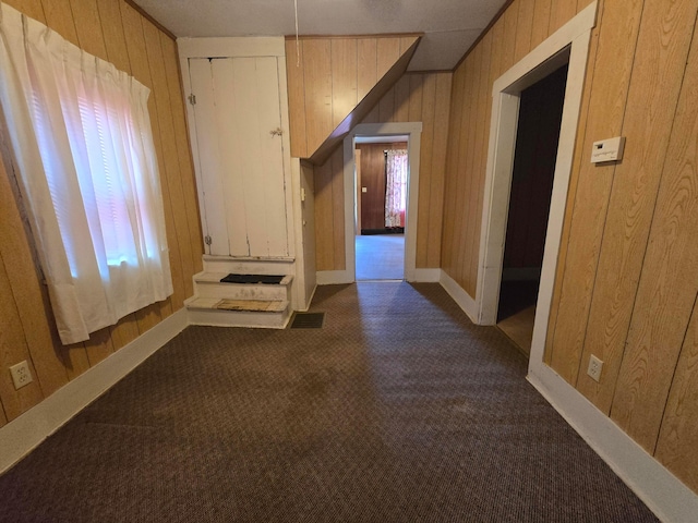 corridor featuring dark carpet and wood walls