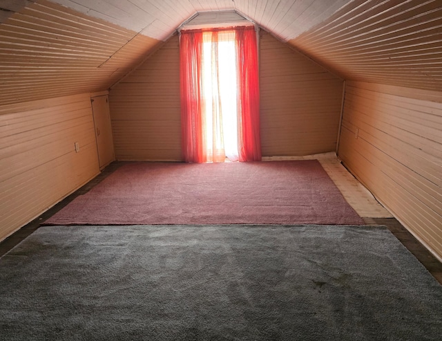 additional living space with dark colored carpet, vaulted ceiling, and wood walls