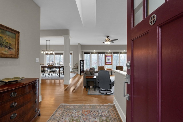 interior space featuring ceiling fan with notable chandelier, a healthy amount of sunlight, light hardwood / wood-style floors, and decorative columns