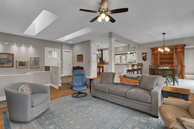 living room featuring ceiling fan with notable chandelier, light hardwood / wood-style floors, and a skylight