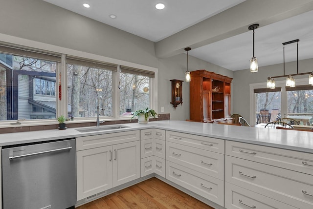 kitchen with sink, white cabinetry, hanging light fixtures, stainless steel dishwasher, and light hardwood / wood-style floors