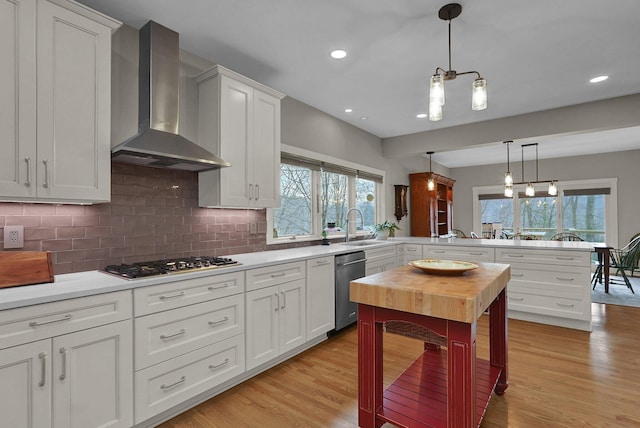 kitchen with pendant lighting, wall chimney range hood, stainless steel appliances, white cabinets, and decorative backsplash