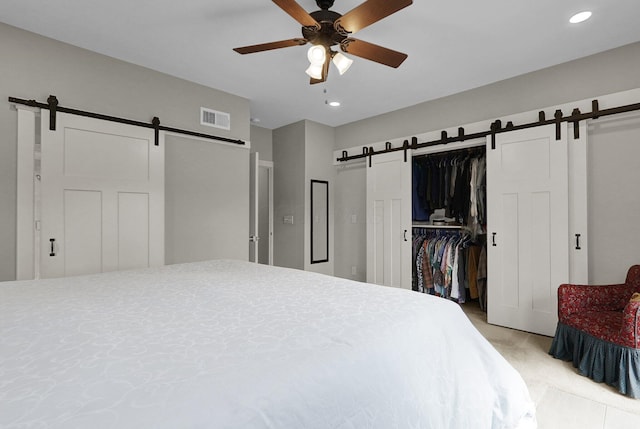 bedroom with a barn door, ceiling fan, and a closet