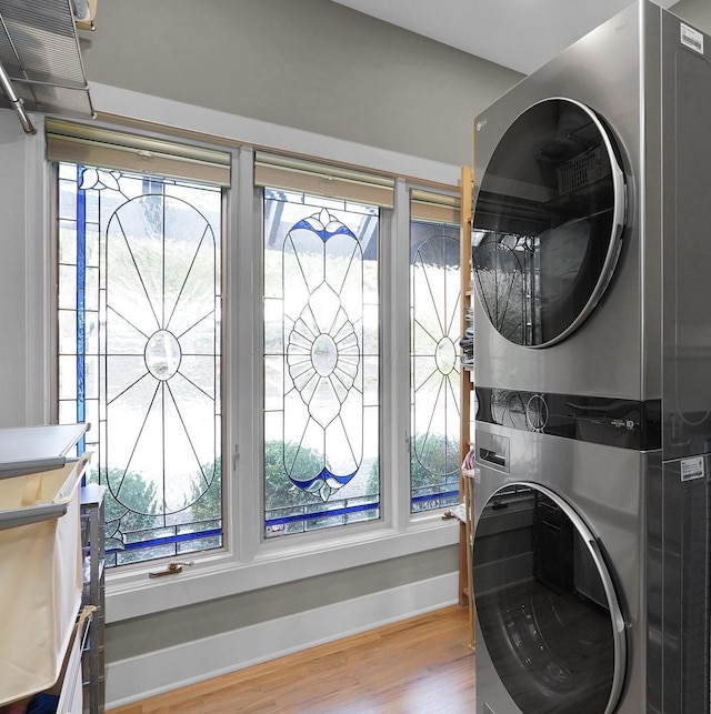 washroom with hardwood / wood-style flooring, stacked washer and clothes dryer, and a healthy amount of sunlight