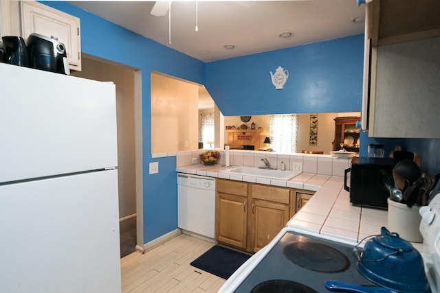 kitchen with tile countertops, sink, white appliances, and light hardwood / wood-style flooring