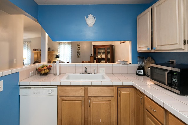 kitchen featuring tile countertops, dishwasher, sink, light brown cabinetry, and kitchen peninsula