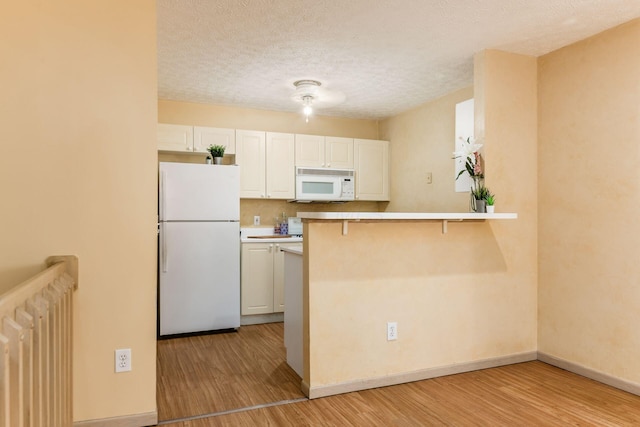 kitchen with light wood-type flooring, radiator heating unit, white appliances, and kitchen peninsula