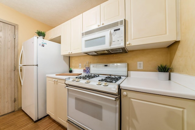 kitchen with a textured ceiling, white appliances, and light hardwood / wood-style floors