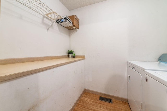 clothes washing area with washing machine and dryer, a textured ceiling, and hardwood / wood-style flooring