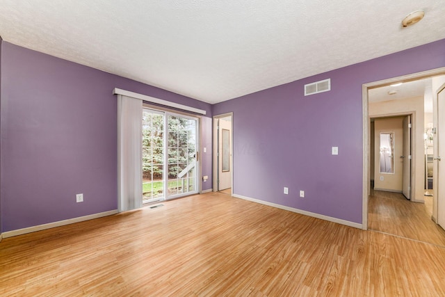 empty room with a textured ceiling and light hardwood / wood-style floors