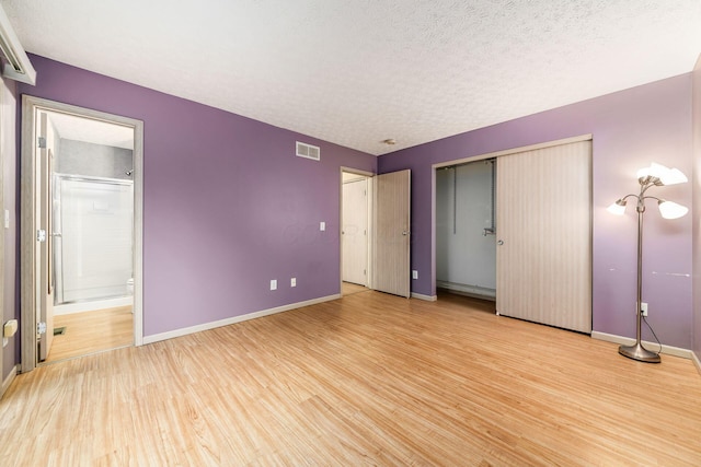 unfurnished bedroom featuring a textured ceiling, connected bathroom, light hardwood / wood-style flooring, and a closet