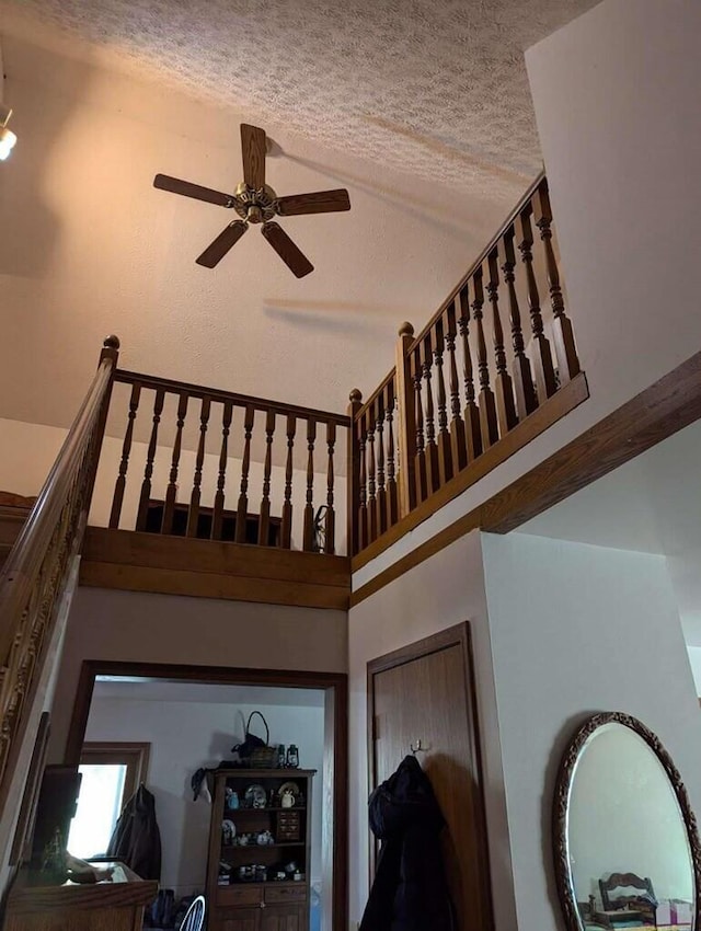 stairs with ceiling fan, a textured ceiling, and a high ceiling