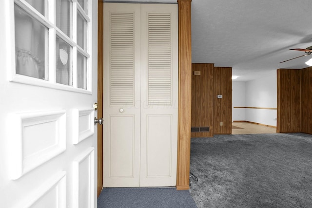 corridor featuring a textured ceiling, carpet floors, and wooden walls