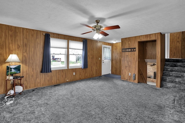 interior space featuring wood walls, ceiling fan, dark carpet, and a textured ceiling